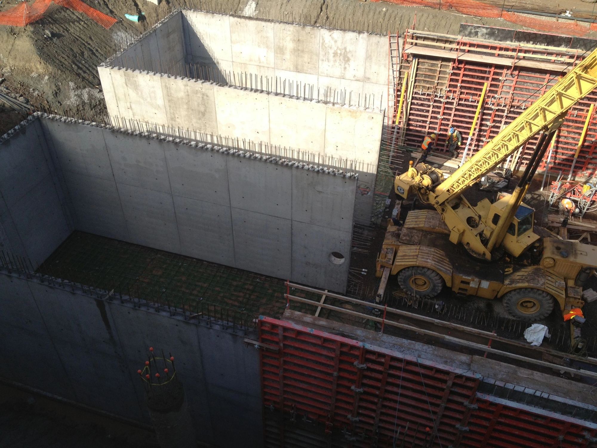 Below-grade foundation walls formed and poured inside a deep excavation, crane on site