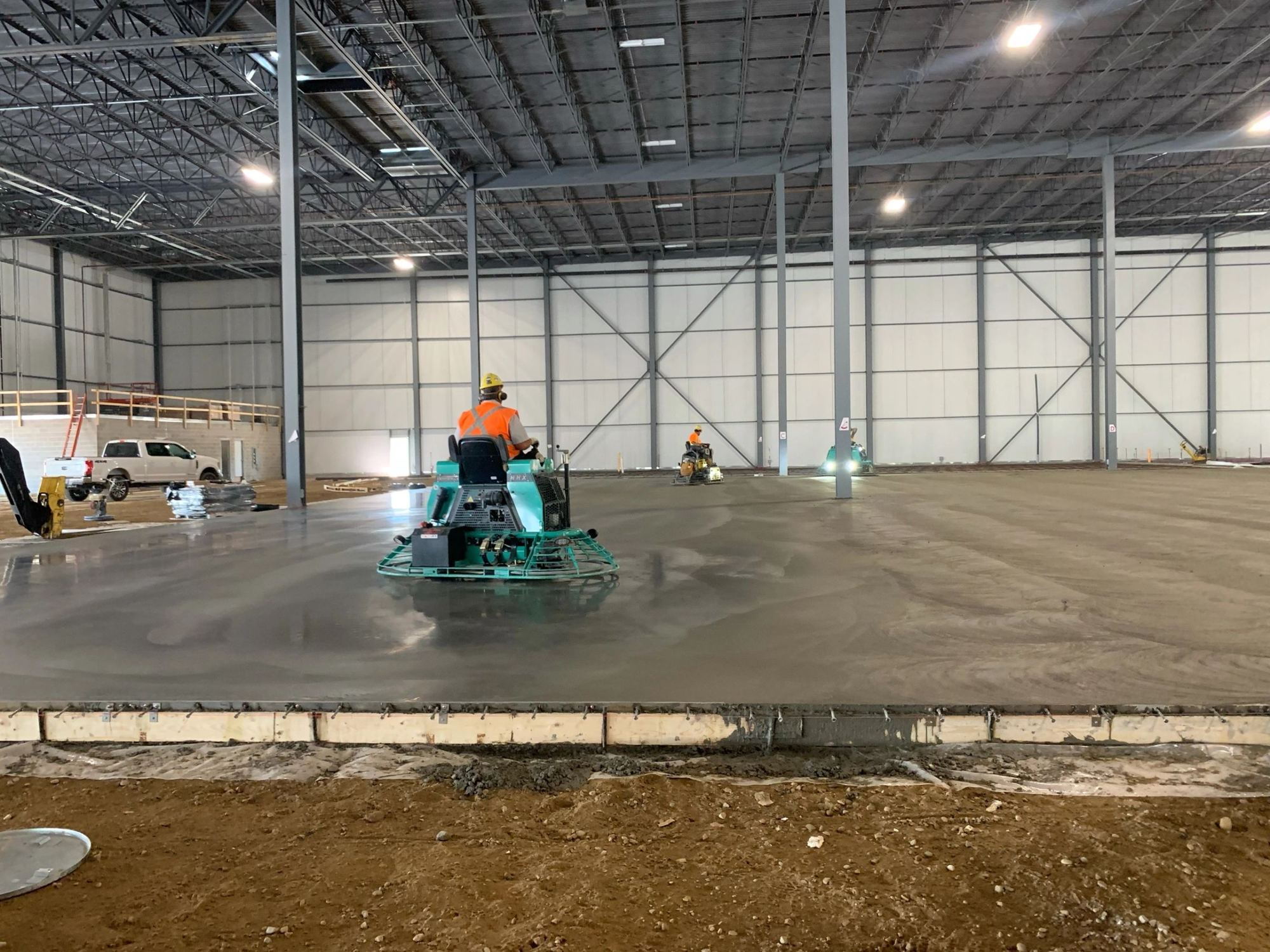 A finisher on a ride-on power trowel working a fresh slab inside a warehouse