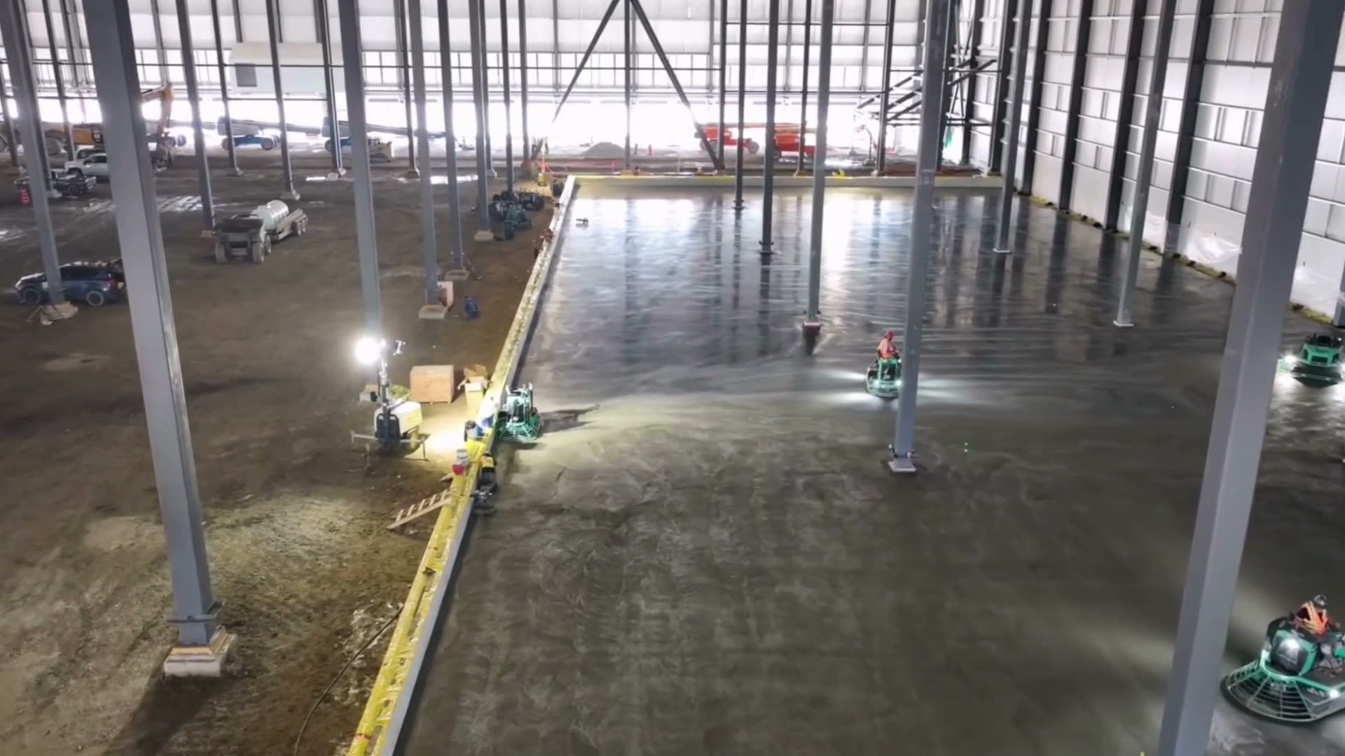 Seen from above, ride-on trowels finishing a warehouse slab under work lights