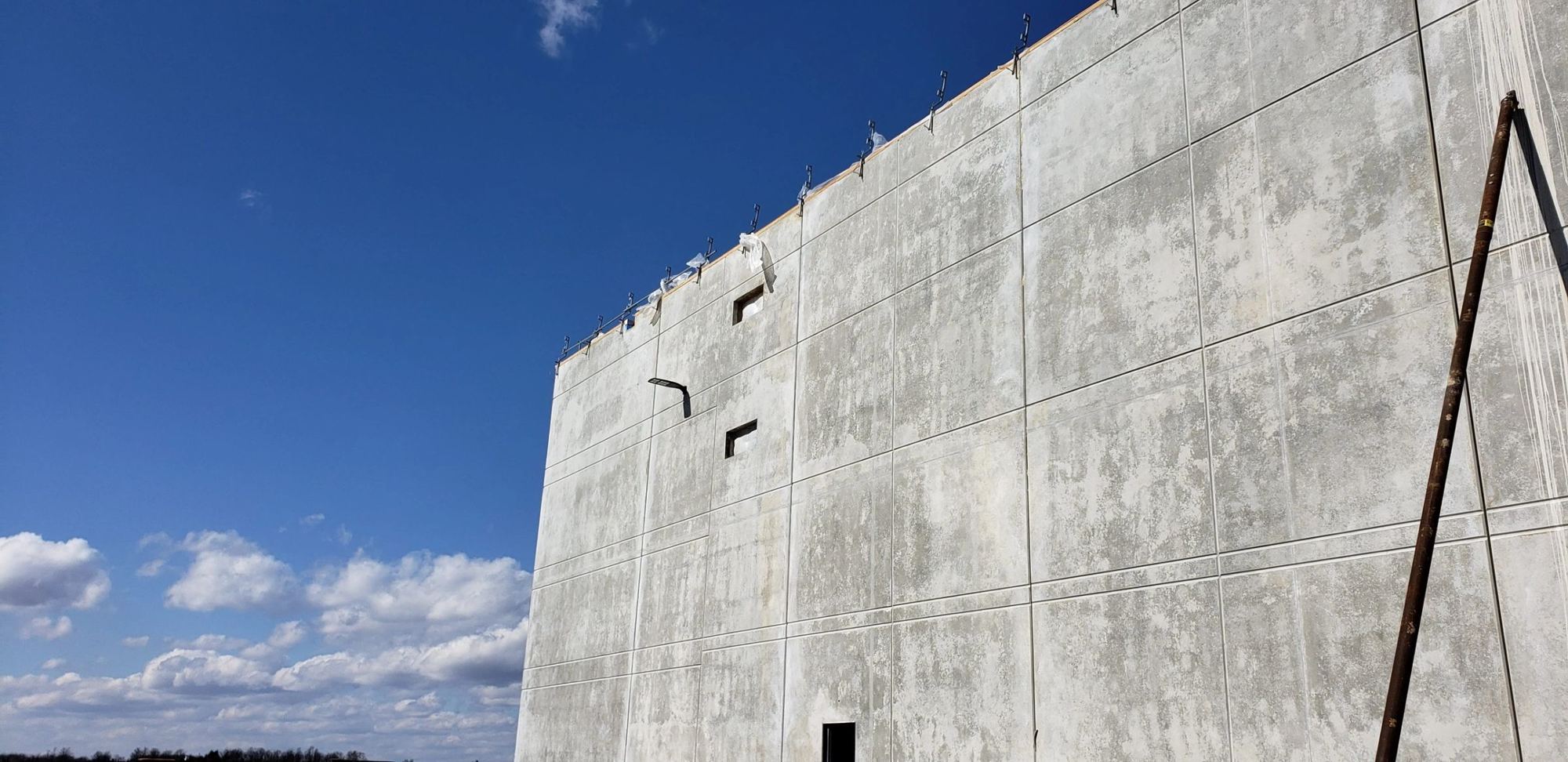 A tall concrete wall rising against a blue sky with braces at its base